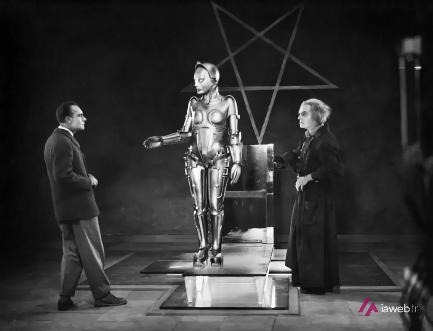 Scène du film Metropolis (1927) : le robot Maria en métal entre deux hommes, devant une étoile à cinq branches